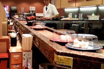 <p>Plates of sushi go around and around in front of you. But you can directly tell the chef what you&#39;d like to eat, then he will make it and hand it to you from inside the counter &nbsp;</p>