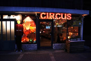 <p>ด้านหน้า Pan &amp; Circus ตอนกลางคืนที่มีสีวันสะดุดตาด้วยไฟหลากสีสัน</p>