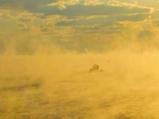 A fishing boat fades in and out of view in a sea of cloud