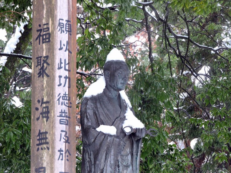 <p>Snow-capped statue of the monk Taicho standing silently on the temple grounds</p>