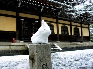 A snow bunny sitting on a marker post in front of the temple