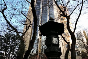 <p>Bronze lantern and bare trees in shadow with the tall Prince Sakura Tower Tokyo in the background</p>