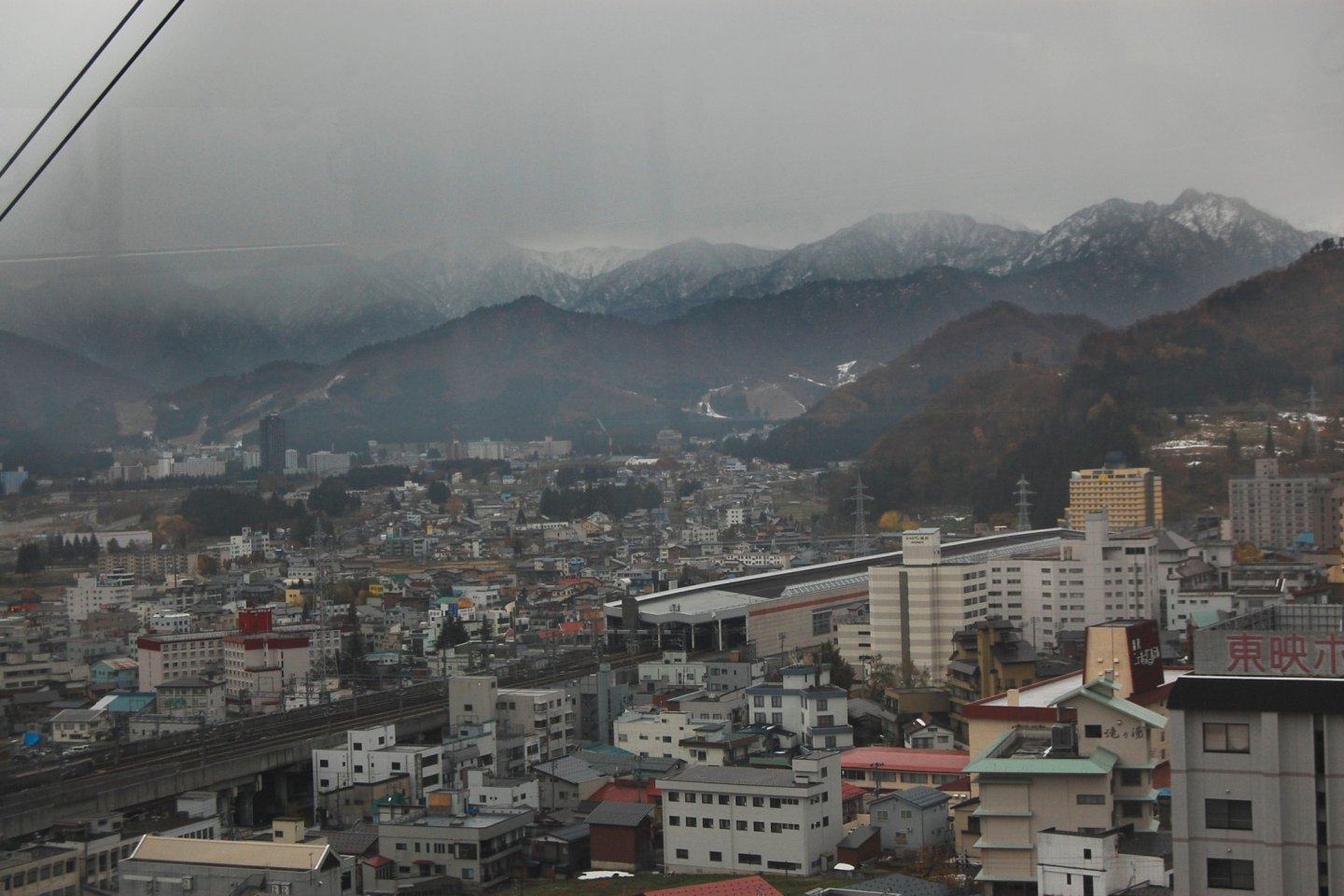 Pemandangan kota Yuzawa dari atas. Terlihat mendung dengan pegunungan bersalju di sekelilingnya.