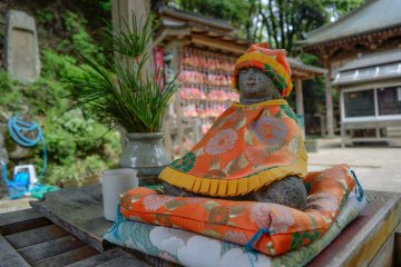 <p>Stone Buddha wearing cute cape and hat</p>