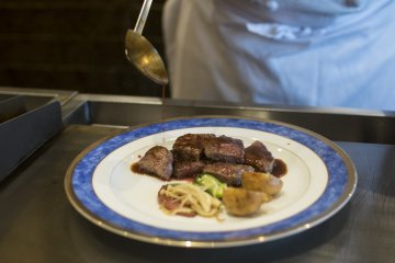 <p>Chef puts on the finishing touches, ladling red wine sauce onto the steak.</p>