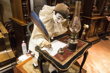 <p>This too is an orgel. Besides playing a hauntingly moving piece, the doll here also moves along to the music, the hand moving to simulate words being scribed onto the paper.</p>