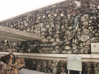 Сзади памятника находится каменная стена, спроектированная архитектором Кэндзи Имаи, изображающая месячное паломничество 26 мучеников из Киото в Нагасаки.