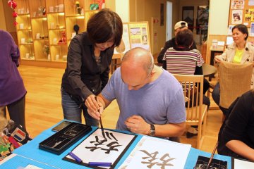 <p>One of the instructors lends a helping hand. The kanji is &quot;tabi,&quot; meaning trip or journey</p>