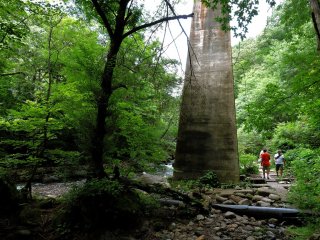 Tall pylons of a rail bridge across the stream tower over sightseers walking the trail