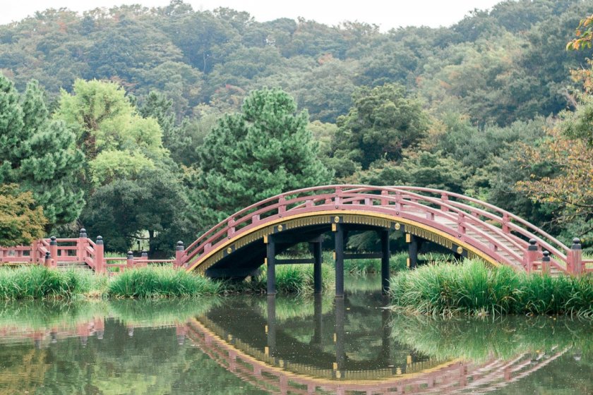 Taman dengan gaya Jodo dengan jembatan melengkung berwarna merah di atas kolam kecil.