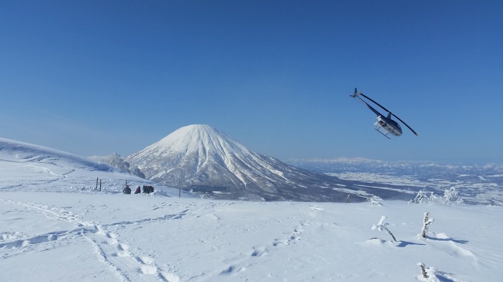 Helikopter lepas landas dari atas dengan Gunung Yotei di latar belakang