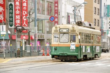 The green tram in front of the busy area of Hatchobori
