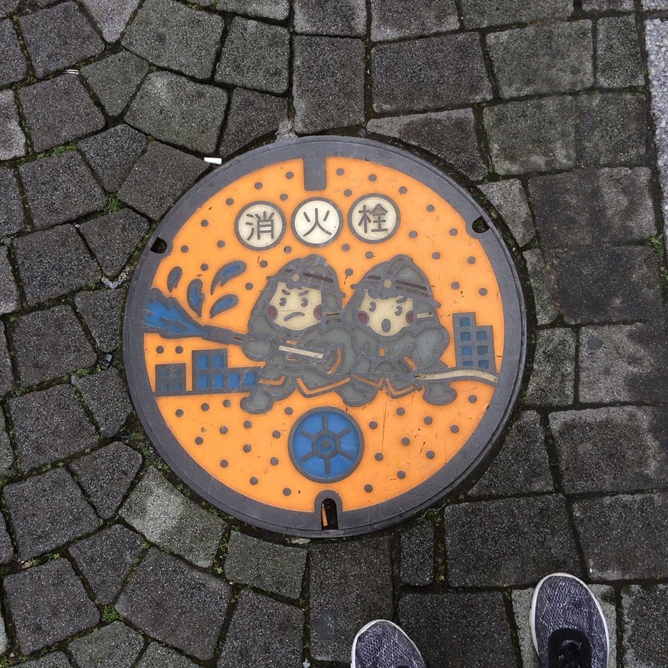 This manhole cover shows firefighters, indicating that a water hydrant is contained within