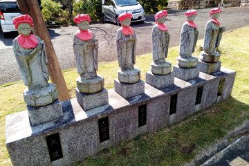 A line of Jizo statues welcome visitors at the parking lot