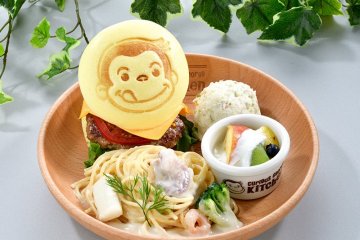 The burger has a Curious George embossed bun and is served with pasta and salads on the side